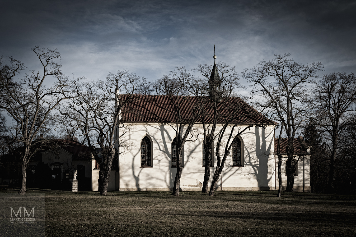 Kostel za stromy v zimě, tmavé mraky.